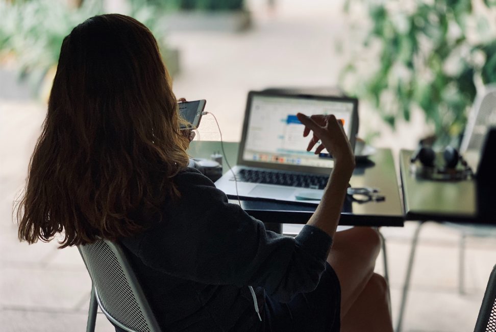 Kvinna sitter framför en laptop och pratar i sin mobiltelefon