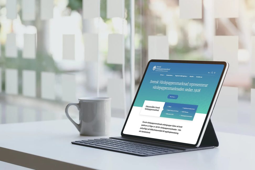 Svensk Värdepappersmarknads nya webbplats visas i en ipad som står på ett bord med en kaffemugg bredvid