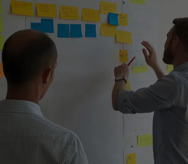 2 män står framför en whiteboard tavla med post it lappar på tavlan