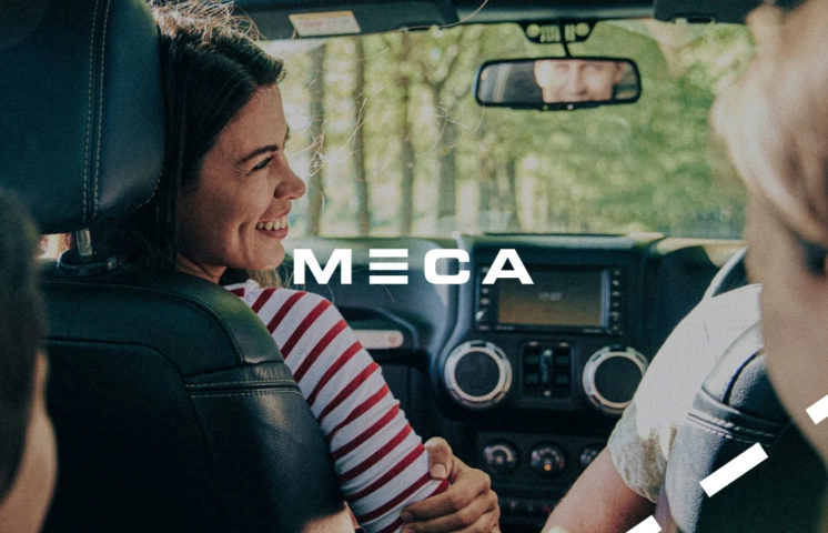 MECAs logga med tillsammans med en leende kvinna som sitter i en bil.